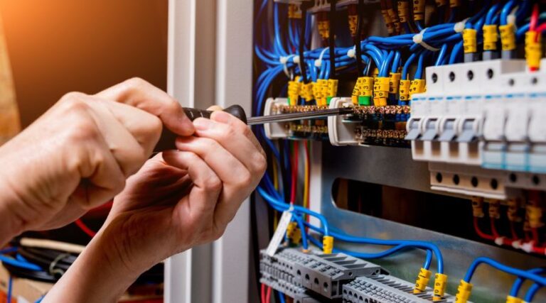 Facility Management Company Electrician using a screwdriver to connect wires in an electrical panel.